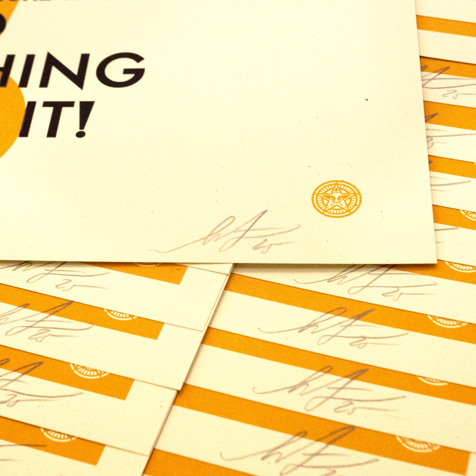 A close-up of the bottom right corner of a poster with a small circular seal and a signature. The poster is surrounded by…