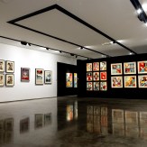 A modern art gallery with white walls on the left displaying framed black and white portraits. A black wall on the right…