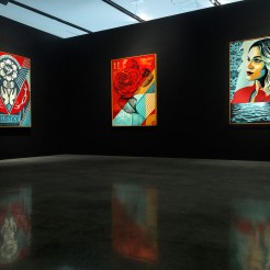 A modern art gallery with a black wall displaying three framed art prints. The prints feature a stylized heart with…