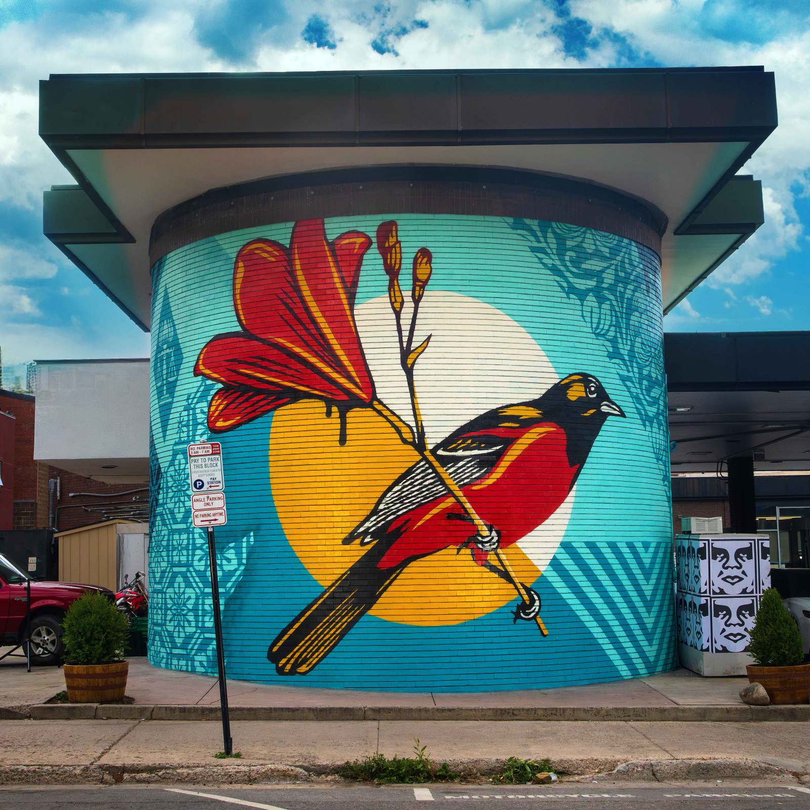 Mural of a bird on a brick building; parking signs visible.