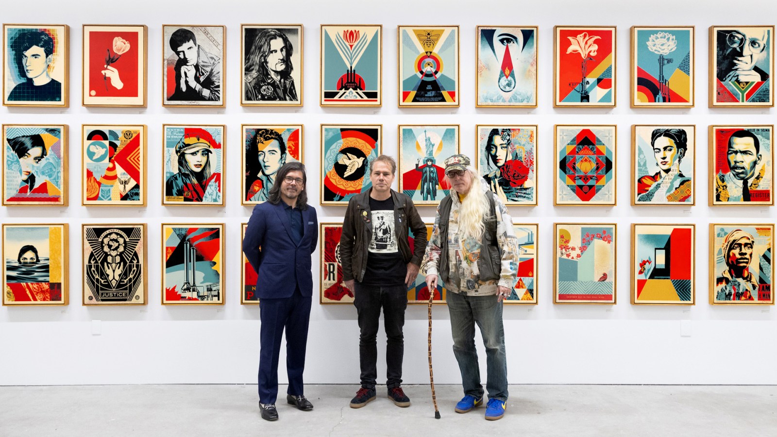 Three men stand before a wall of framed Shephard Fairey prints.