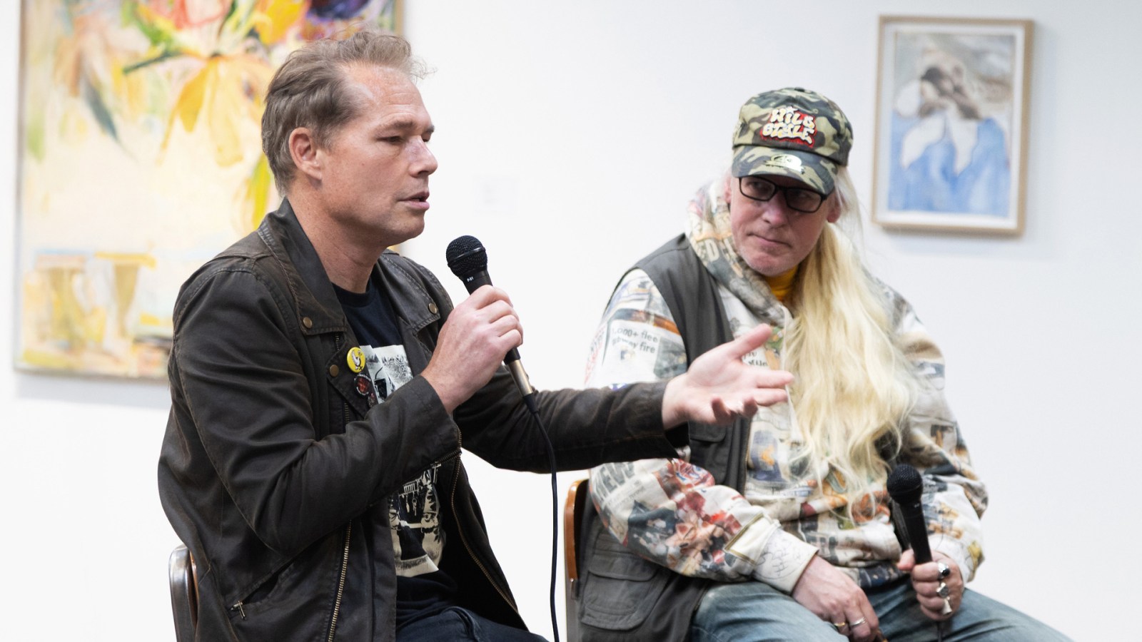 Two men participate in a panel discussion; one holds a microphone.