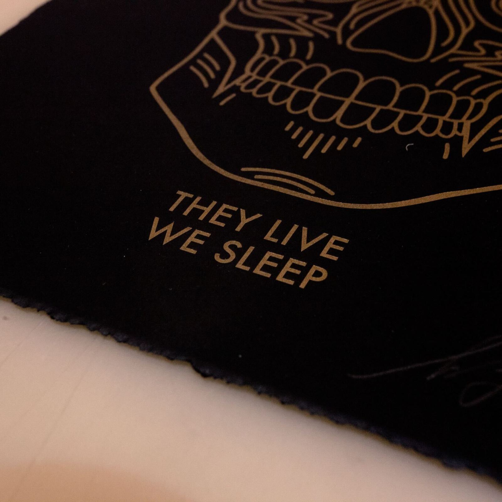 Black print with gold skull graphic and text: They Live We Sleep.