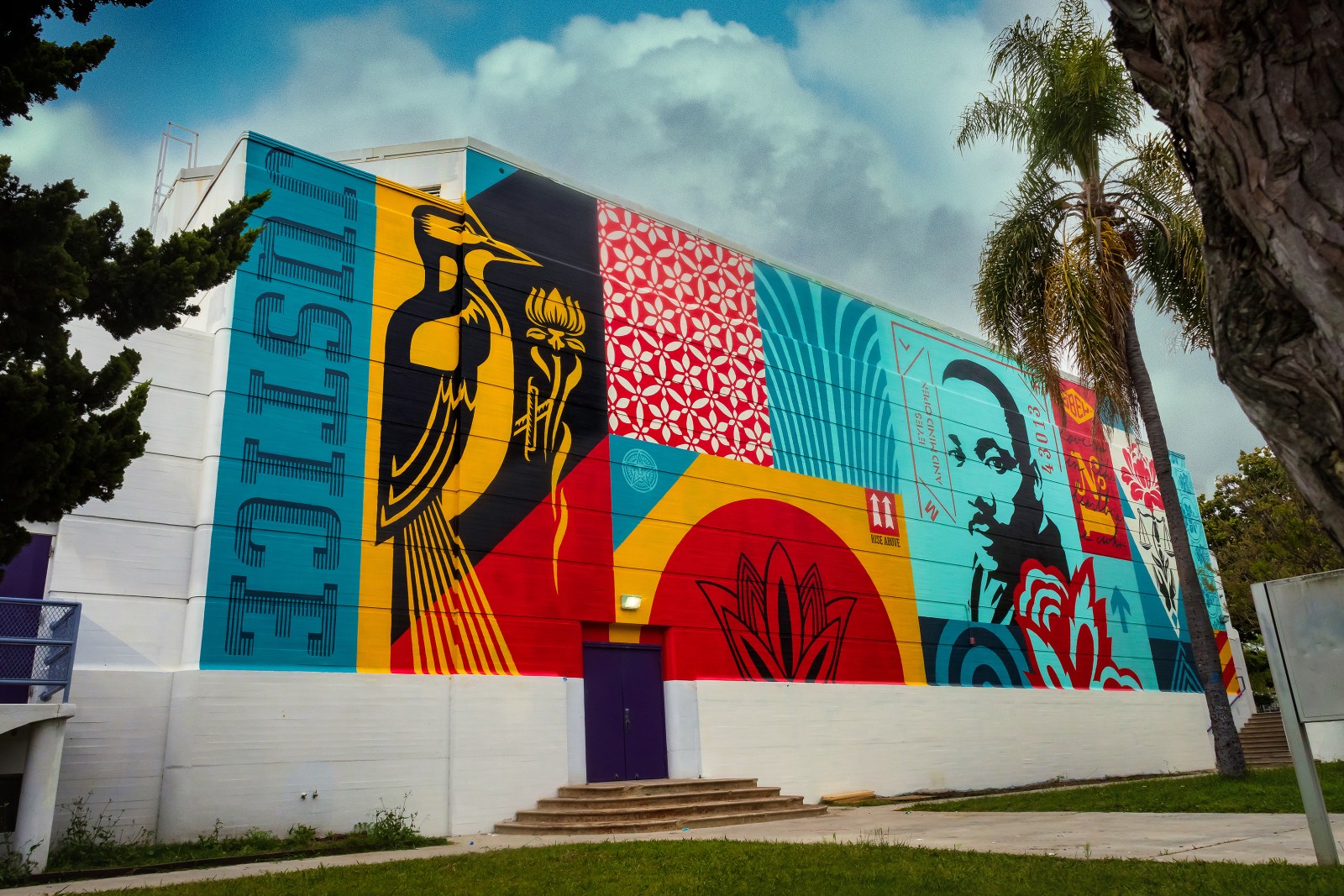 A vibrant mural on a building featuring a bird, Martin Luther King Jr.'s portrait, and various patterns in red, blue…