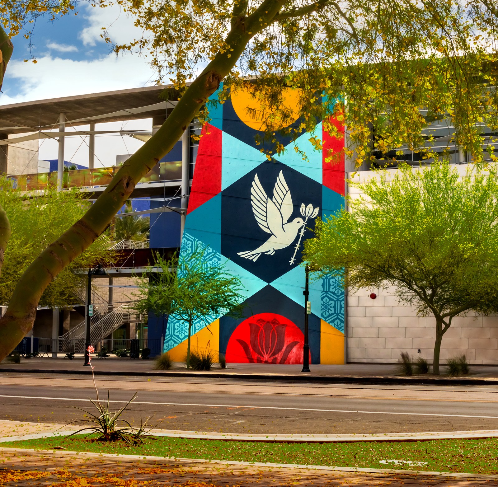 A vibrant mural on a building featuring geometric patterns and a white dove holding a branch, in red, yellow, blue, and…
