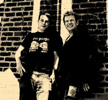Sepia-toned photo of two men against a brick wall; one wears a Sex Pistols t-shirt.