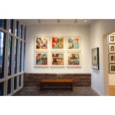 Art gallery with large windows, a brick wall, and a wooden bench, featuring six framed artworks with geometric and floral…