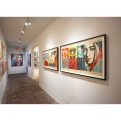 Art gallery hallway with brick floor and white walls, featuring two large framed artworks with female faces and floral…
