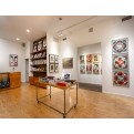 Art gallery with light wood floors, white walls, and various framed artworks, including an "OBEY" poster and a set of four…