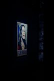 A dimly lit gallery with a single illuminated poster of Kamala Harris in blue and white, with the word "FORWARD" below her.