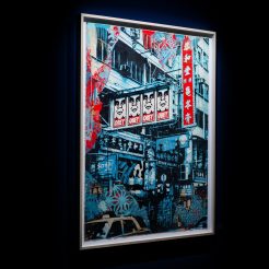 A framed artwork depicting a busy city street scene with buildings, signs, and cars, in blue, red, and white, with "OBEY"…
