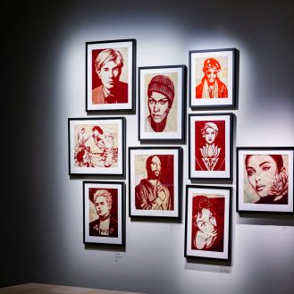 A gallery wall with a grid of nine framed pop art portraits in red and white, featuring various figures including Andy…