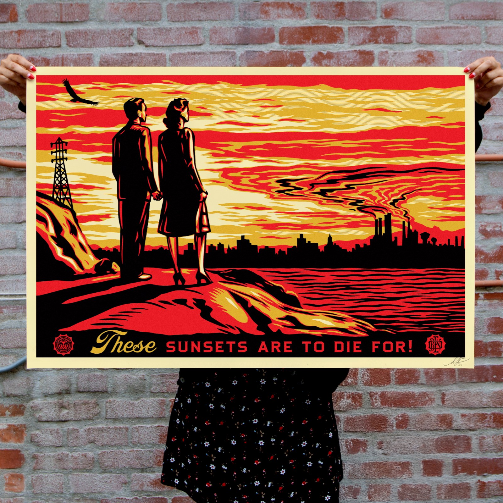 A person holds a poster depicting a couple watching a fiery sunset over an industrial city. Text: THESE SUNSETS ARE TO DIE…