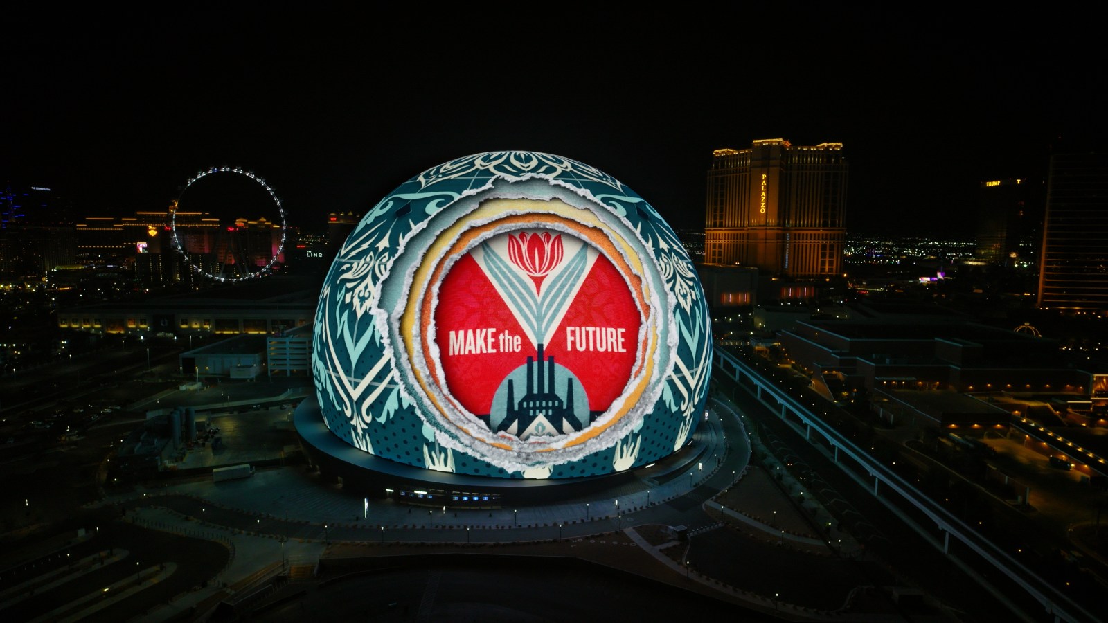 An aerial view of a large spherical building illuminated with a red and white floral design and the text