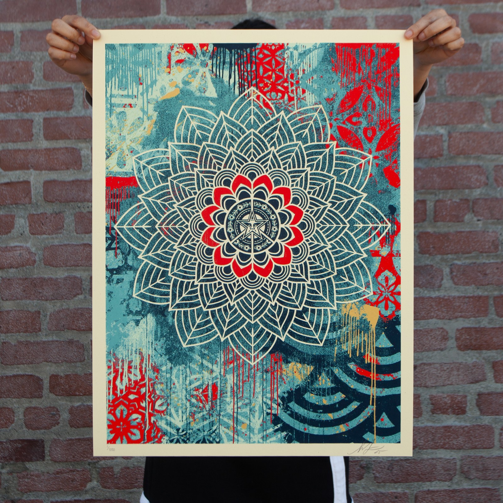 Hands holding a vibrant pop art print featuring a detailed mandala design in blue, red, and cream with distressed textures…