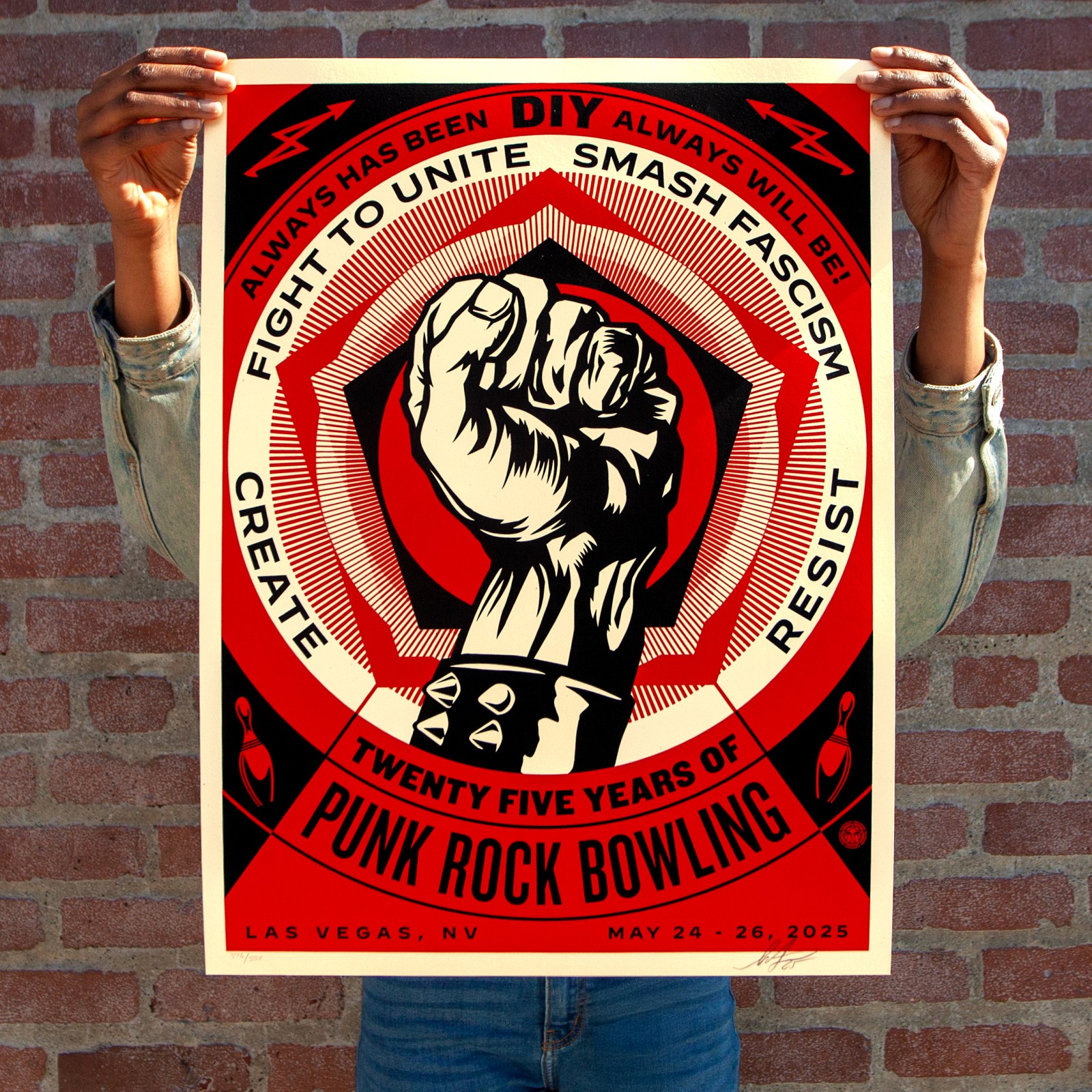 A person holds a red, black, and white poster with a raised fist in the center, surrounded by text: "ALWAYS HAS BEEN DIY…