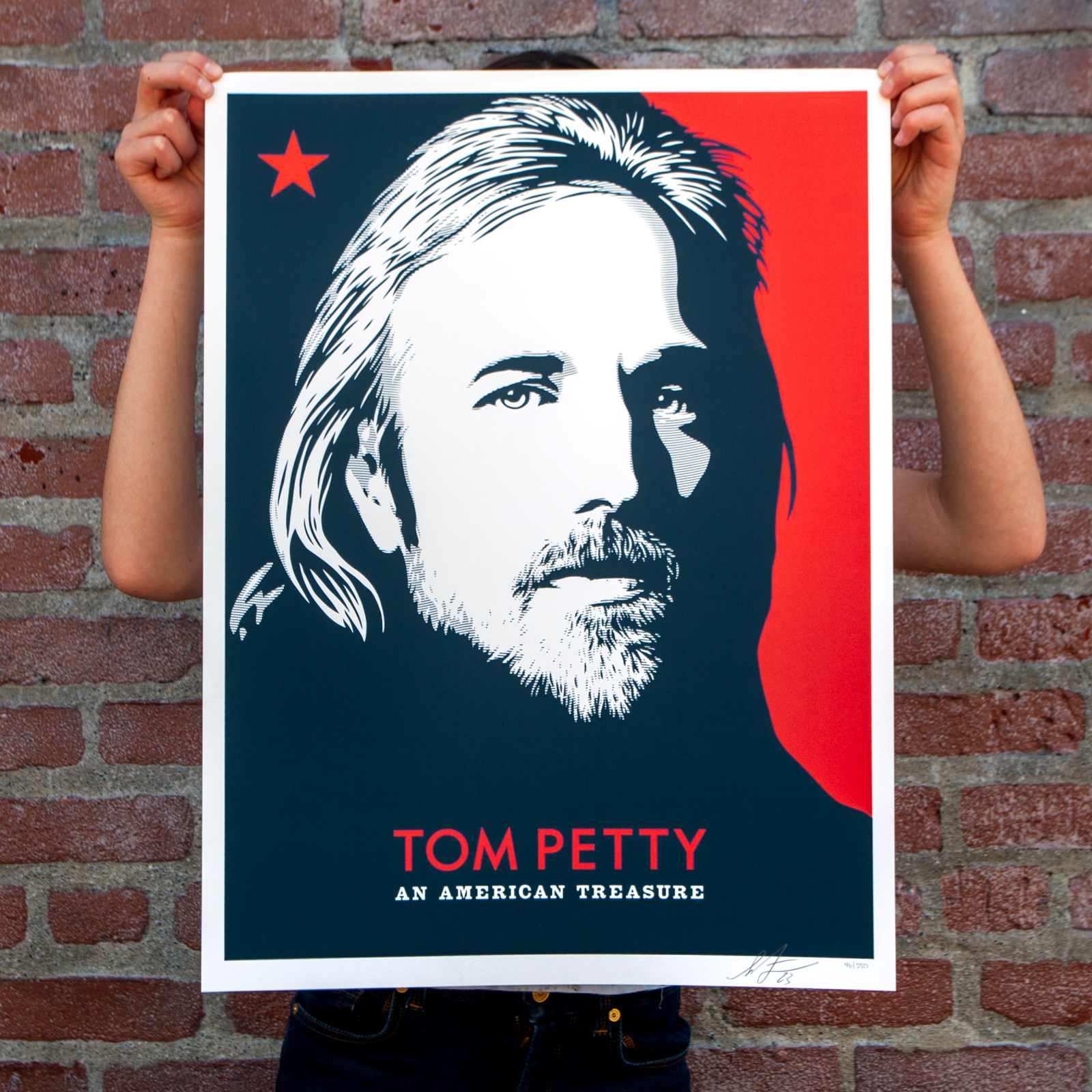 Hands holding a pop art print of Tom Petty's portrait in black, white, and red, with text