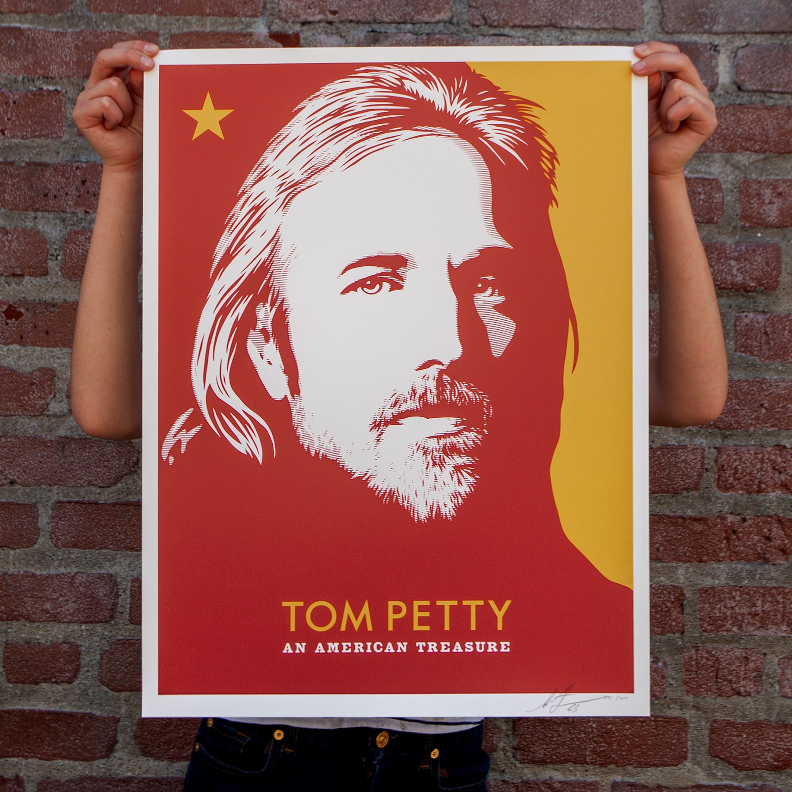 Hands holding a pop art print of Tom Petty's portrait in black, white, and red, with text