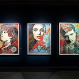 A row of framed artworks on a dark blue wall, featuring portraits of women and men in various styles.