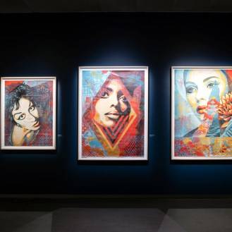 A row of framed artworks on a dark blue wall, featuring portraits of women in various styles.